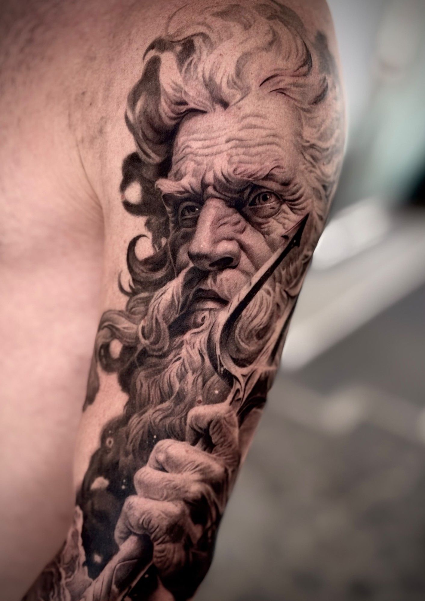 Poseidone con barba e tridente, tatuaggio realistico in bianco e nero sul braccio